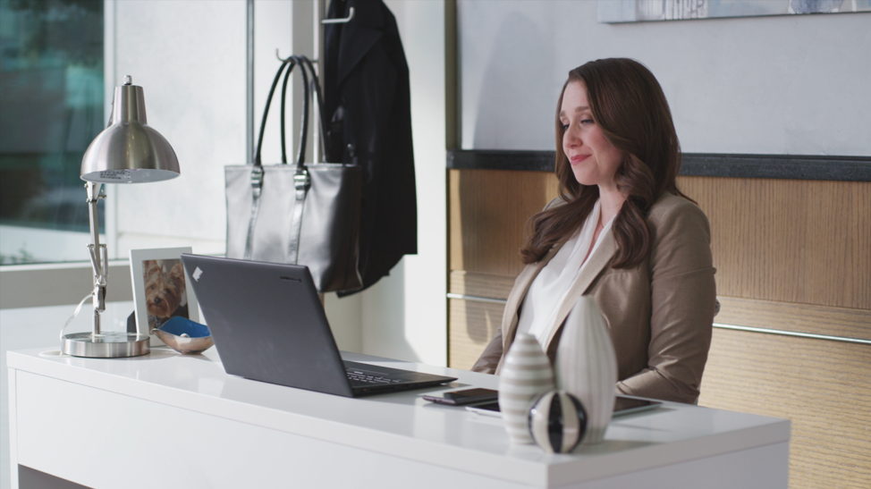 Woman with long brown hair looking at laptop computer in an office setting with natural light pouring in from the window