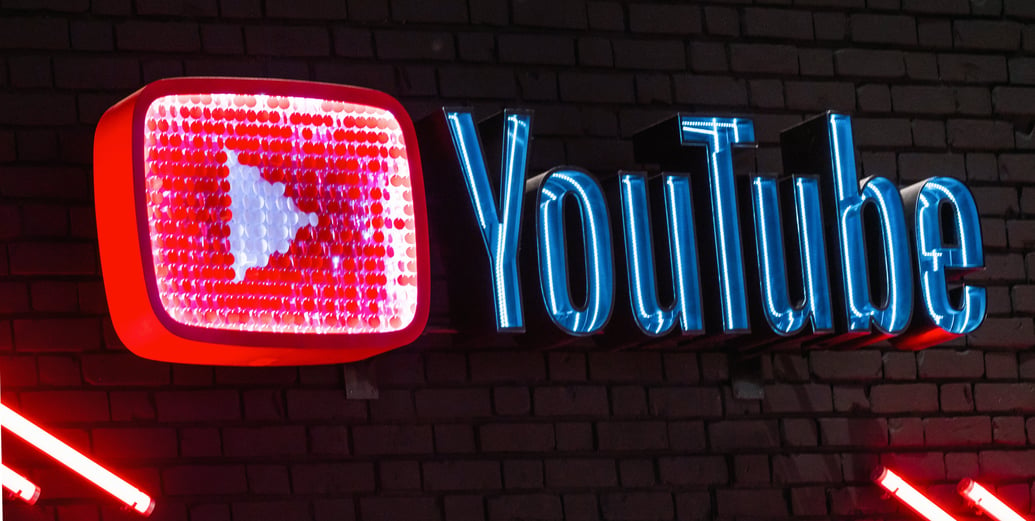 YouTube logo illuminated in neon colors along a brick wall