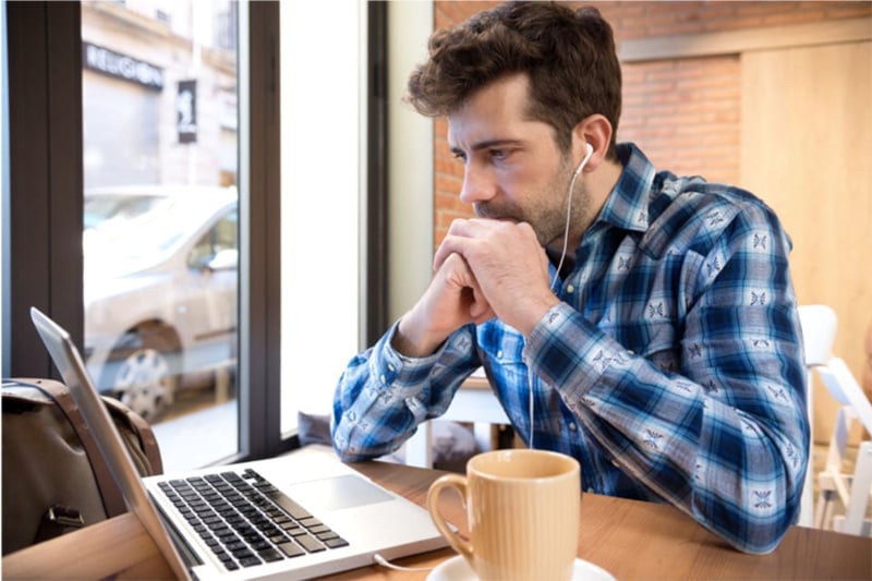 Man wearing headphones watching video on his laptop in a coffee shop setting