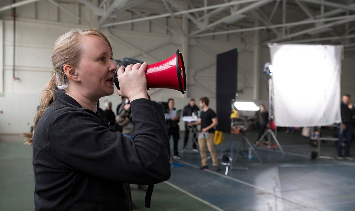 Woman serving as an assistant director holding a megaphone calling for another take on a video production shoot in a warehouse setting