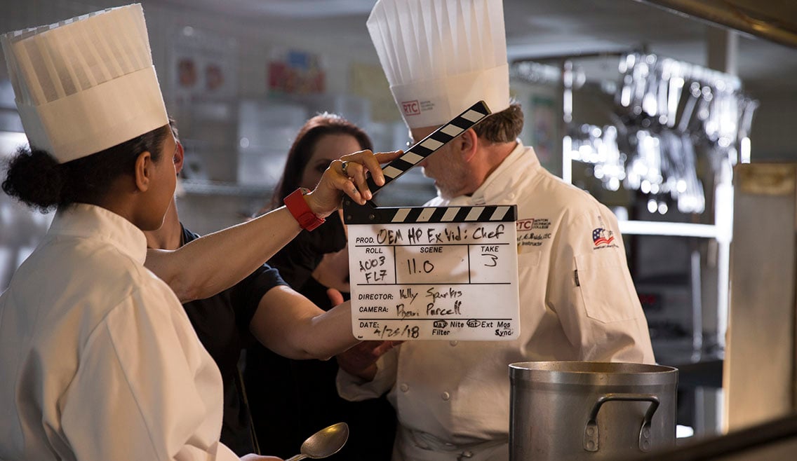 Production assistant holds up a slate for a video production shoot featuring on-camera talent as chefs