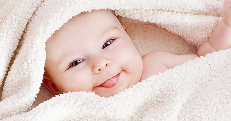 Baby wrapped in blanket looking at camera with tongue sticking out