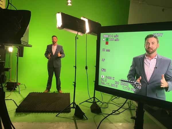 Man standing in front of a green screen in a studio in front of a camera and lights