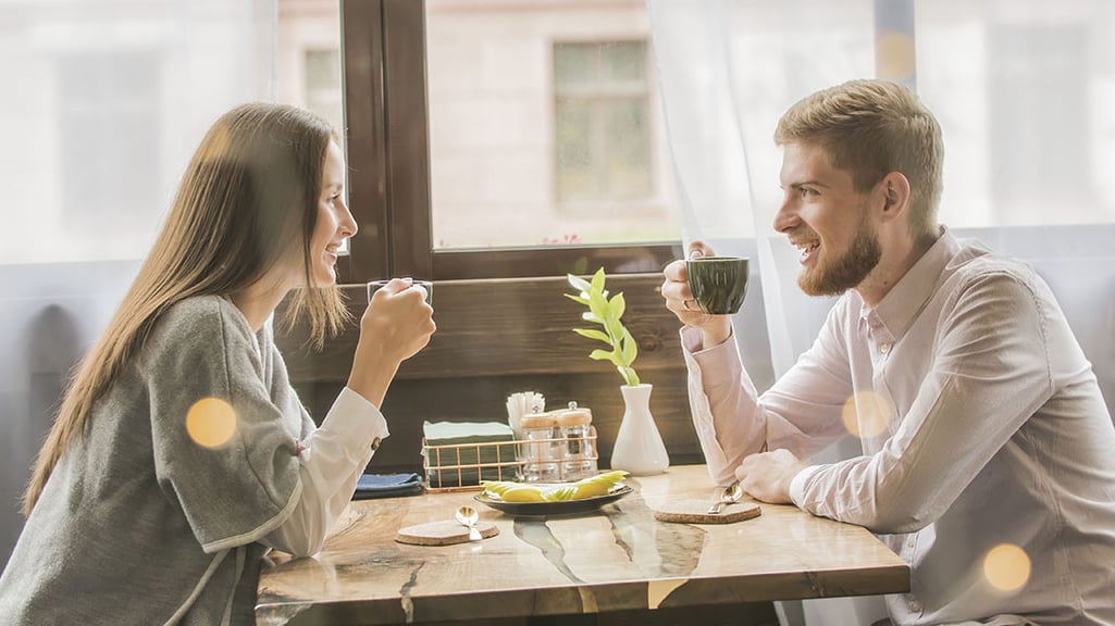 Man and woman drinking coffee in a coffee shop sitting next to a window