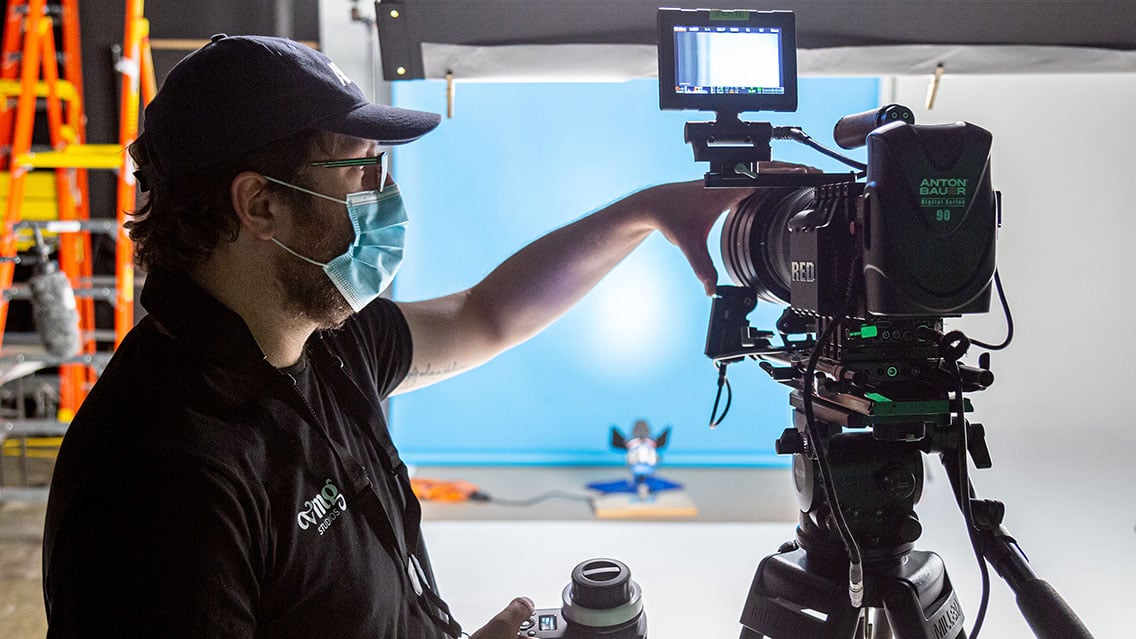 Director of Photography/camera operator wearing a cloth mask shooting in-person video content in-studio during COVID-19