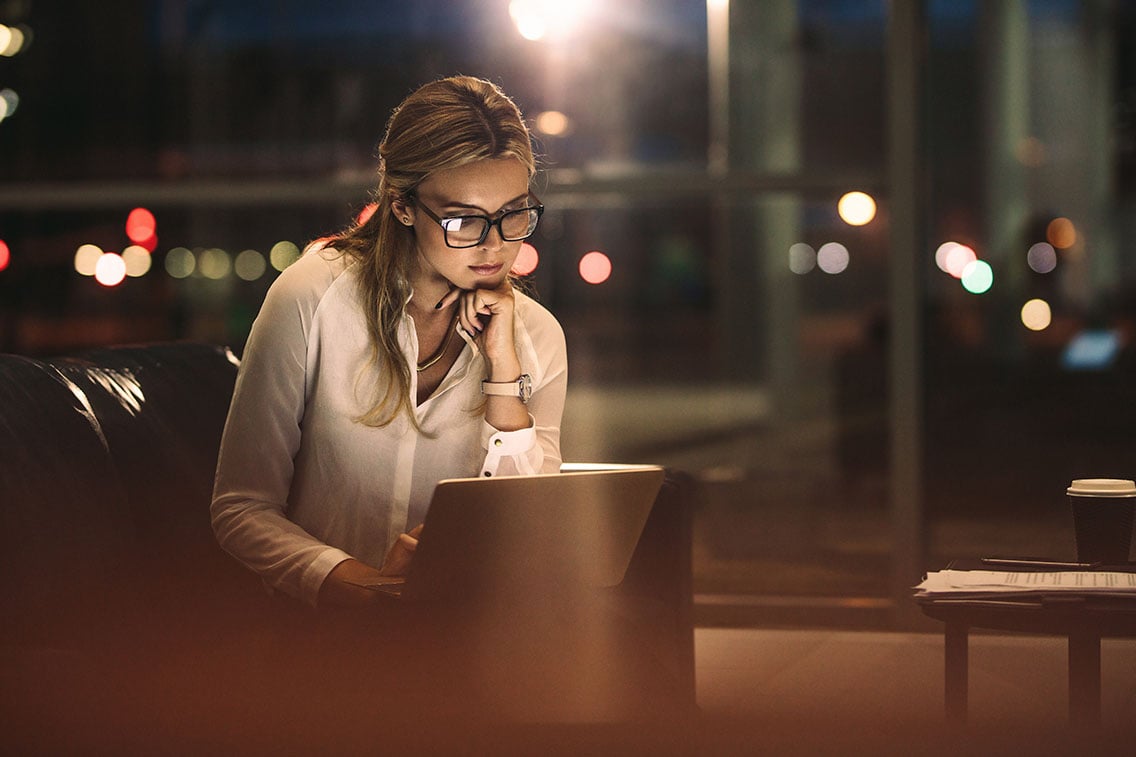 Woman wearing glasses on her computer in a dimly, warm-lit area