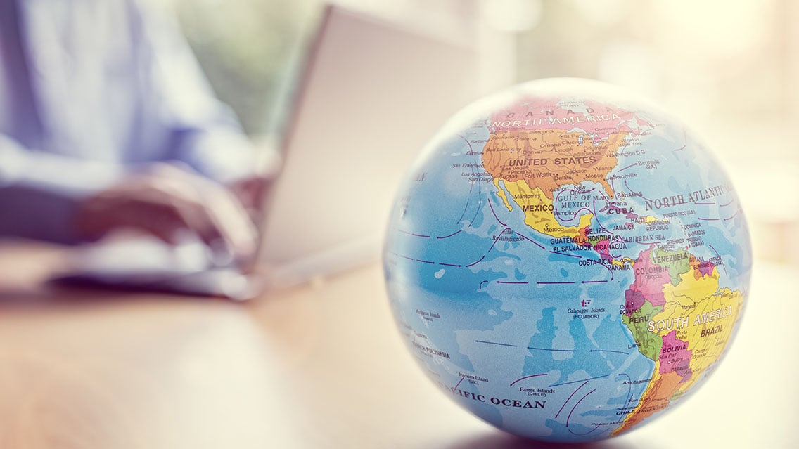 A globe sitting on a desk with a person on a laptop in the background