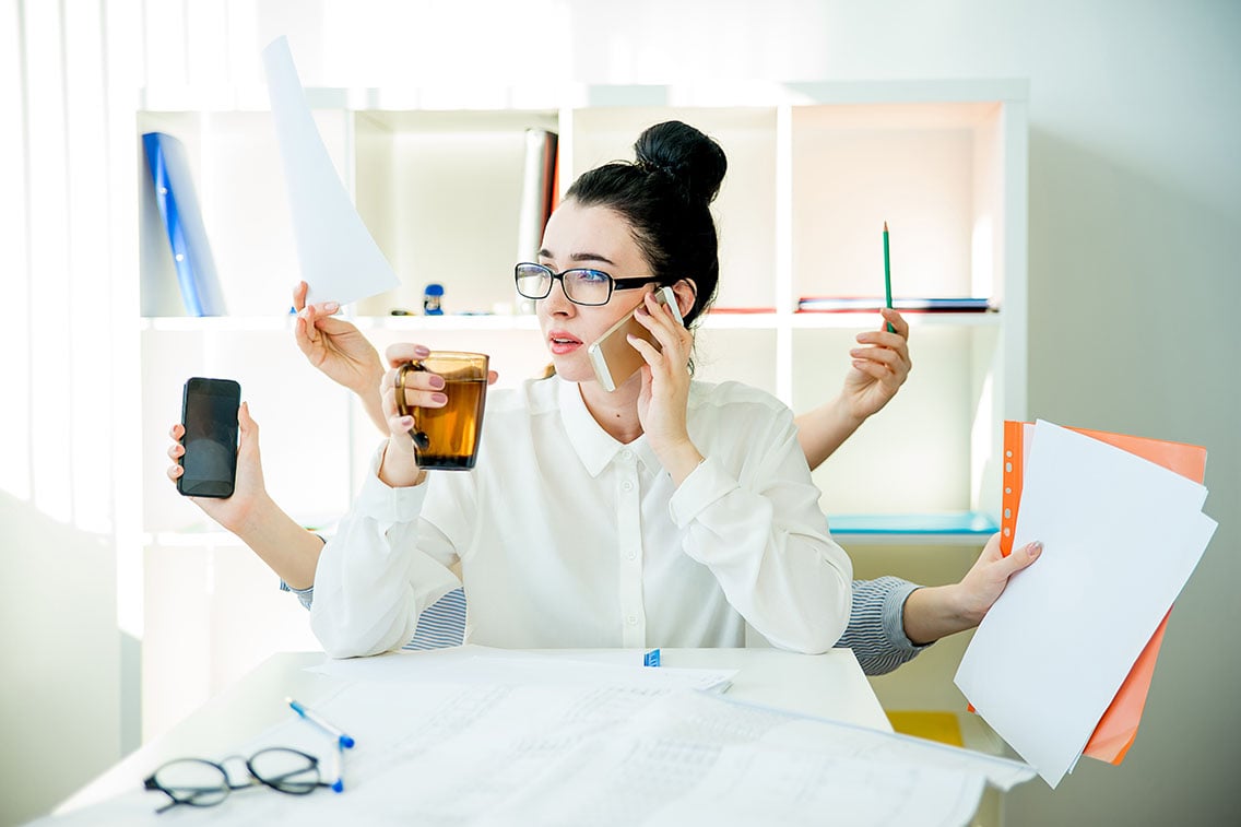 Woman trying to multitask with multiple arms holding work materials like a cell phone, pencil, paperwork