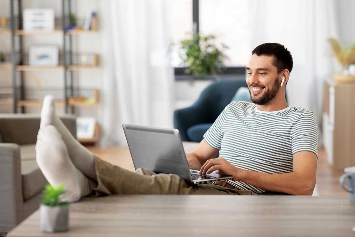 Man with airpods in listening to music while on his computer with his feet up on his clean desk workspace