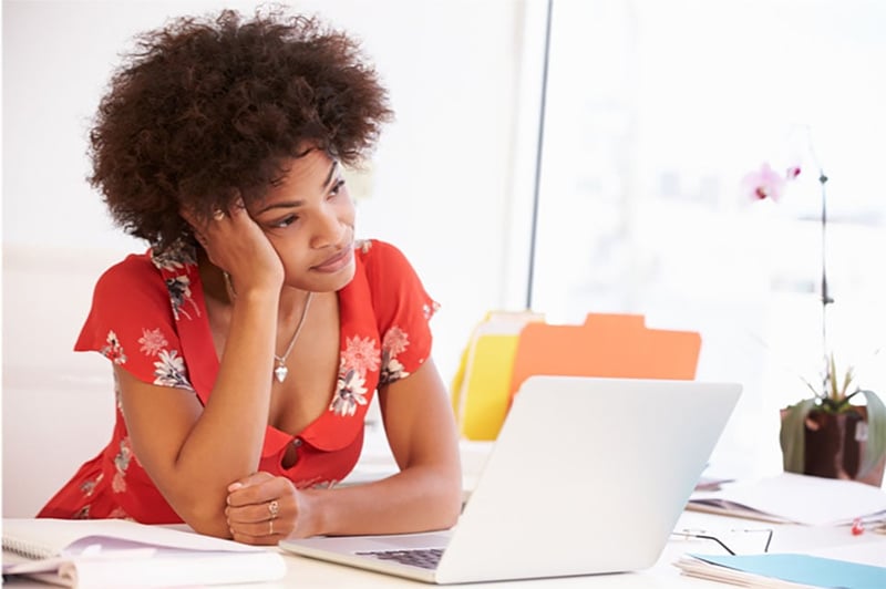 Woman looking bored in office setting trying to pay attention to a video playing on her laptop