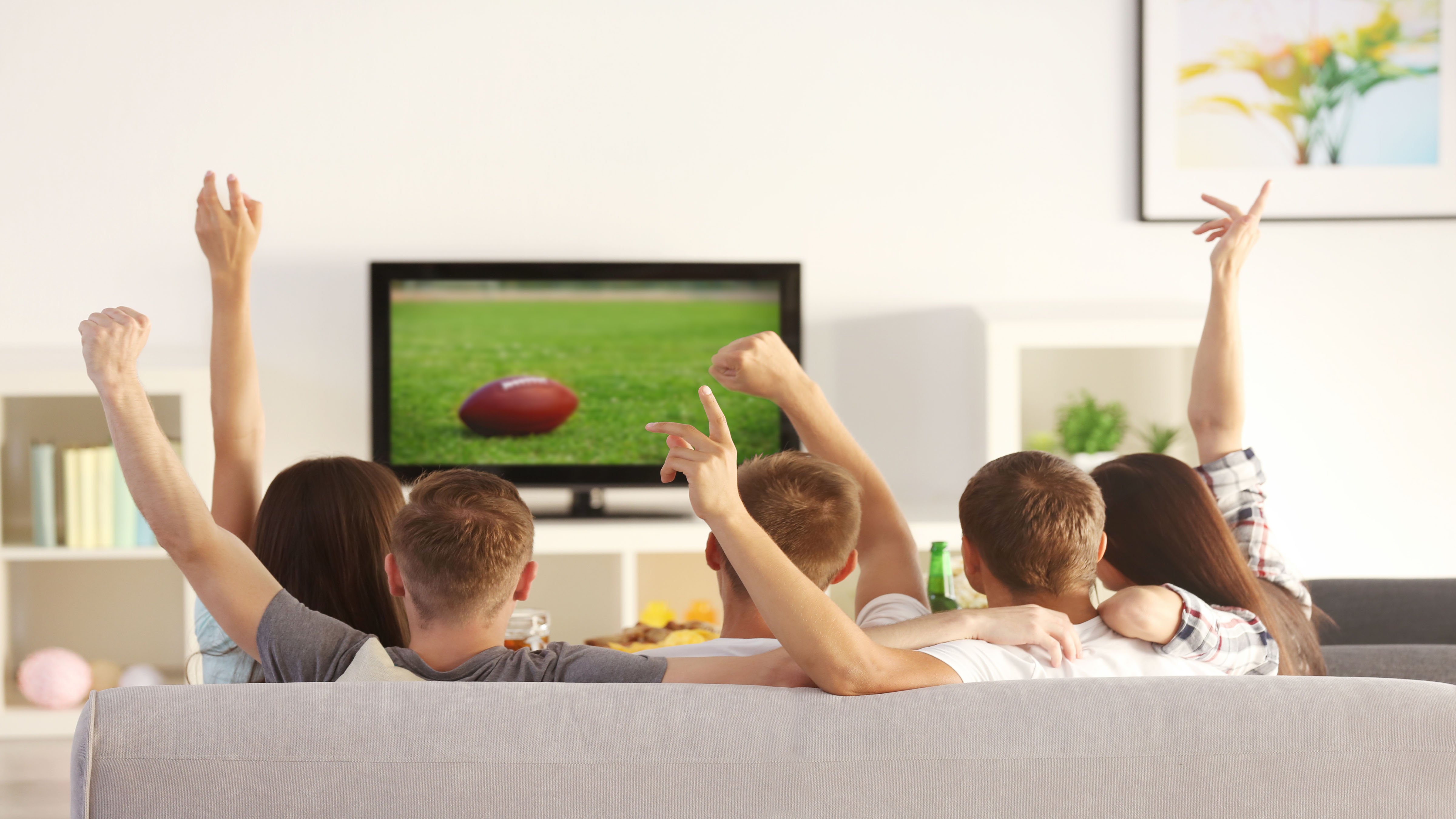 5 people sitting on a couch watching football on TV