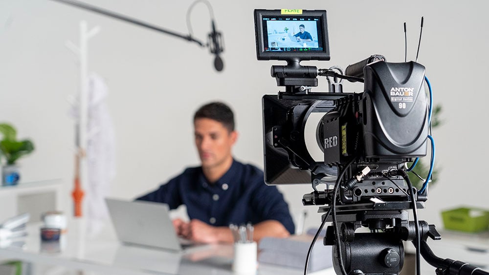 Behind the scenes look of a male actor on a laptop with the camera focused on his office setting