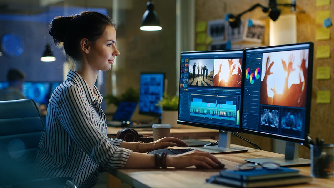 Woman editing a video in its post-production stage on two computer monitors 